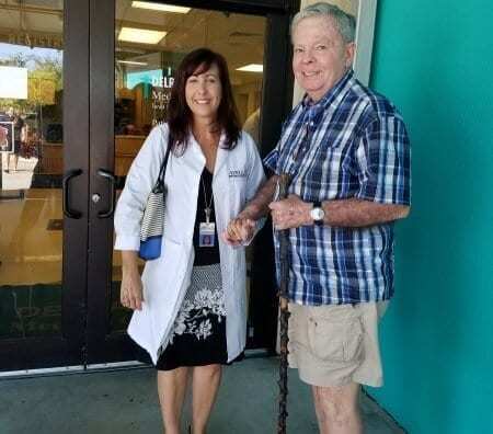 An elderly man with a cane and doctor standing in front of a building